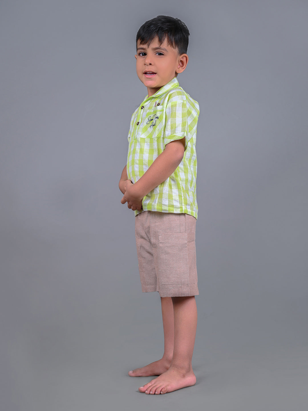 A boy wearing lime green drop shoulders shirt and beige linen shorts