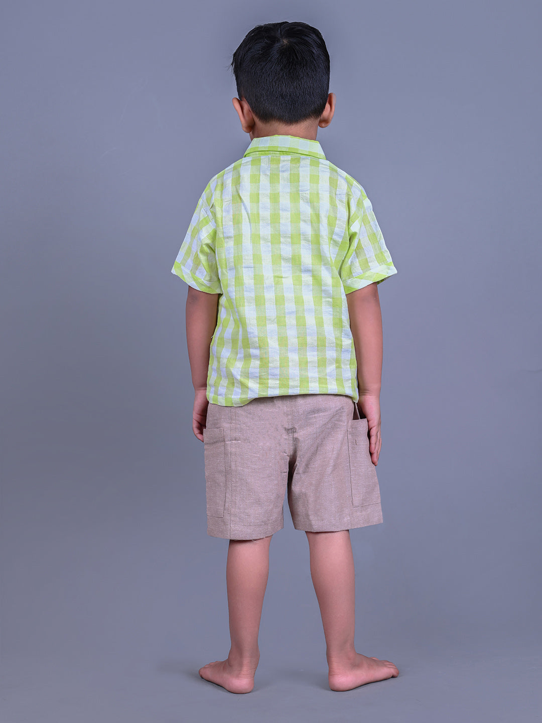 A boy wearing lime green drop shoulders shirt and beige linen shorts